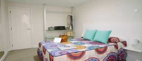 A bedroom with a bed, a laptop, a handbag, and a shelf with clothes and a radio.