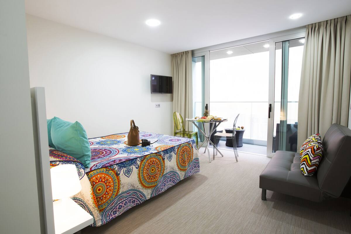 A modern hotel room with a bed, a sofa, a small table, and a TV.