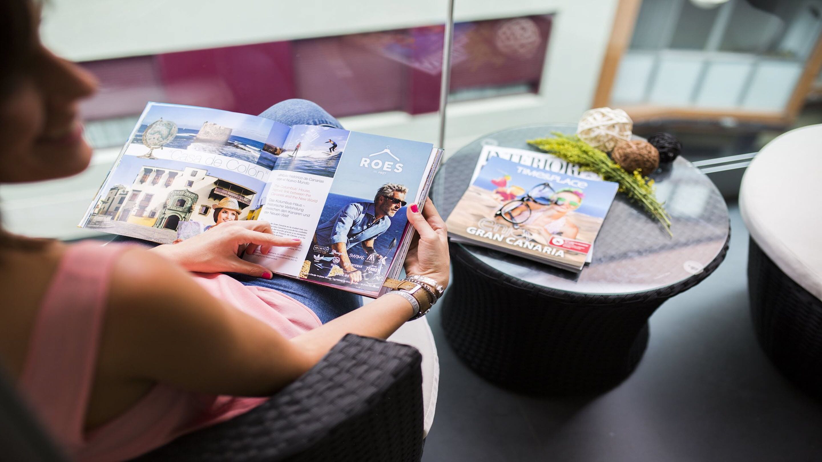 Iemand bekijkt een reisbrochure met afbeeldingen van een kustplaats en een tijdschrift met de titel 'GRAN CANARIA'.