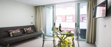 A modern living room with a sofa, a glass dining table, and a TV mounted on the wall.