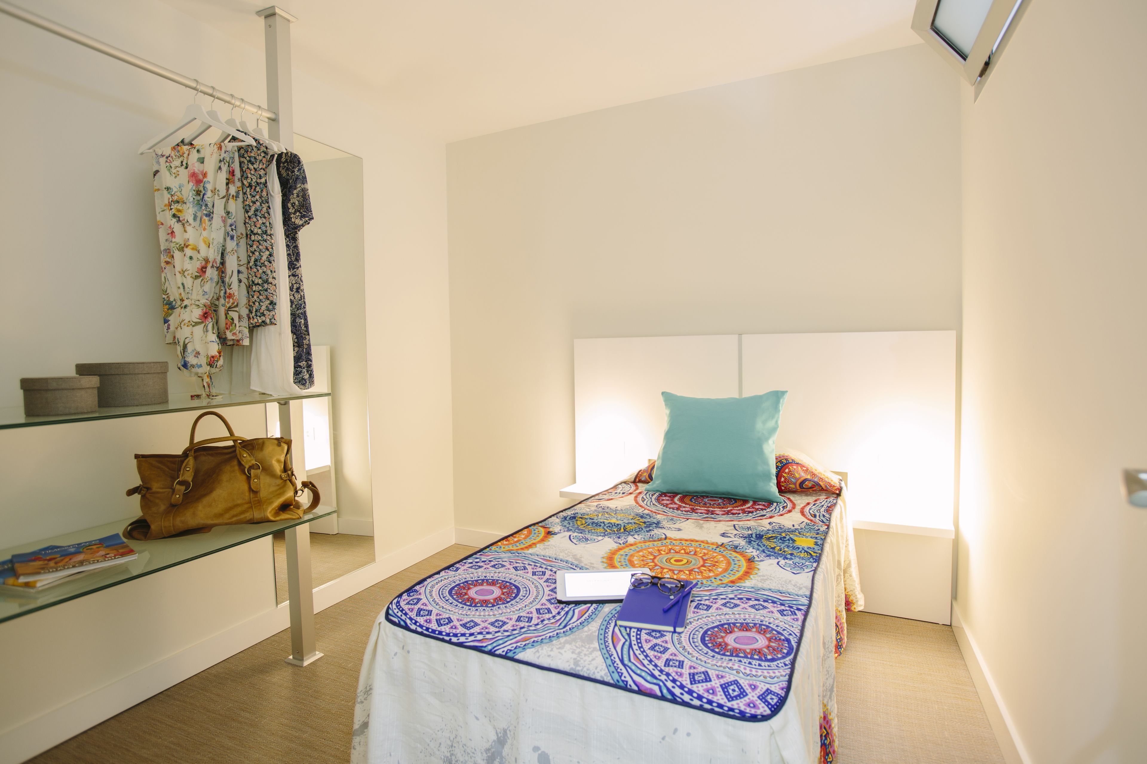 A small, neatly arranged bedroom with a bed, a shelf with a handbag, and a hanging rack with clothes.