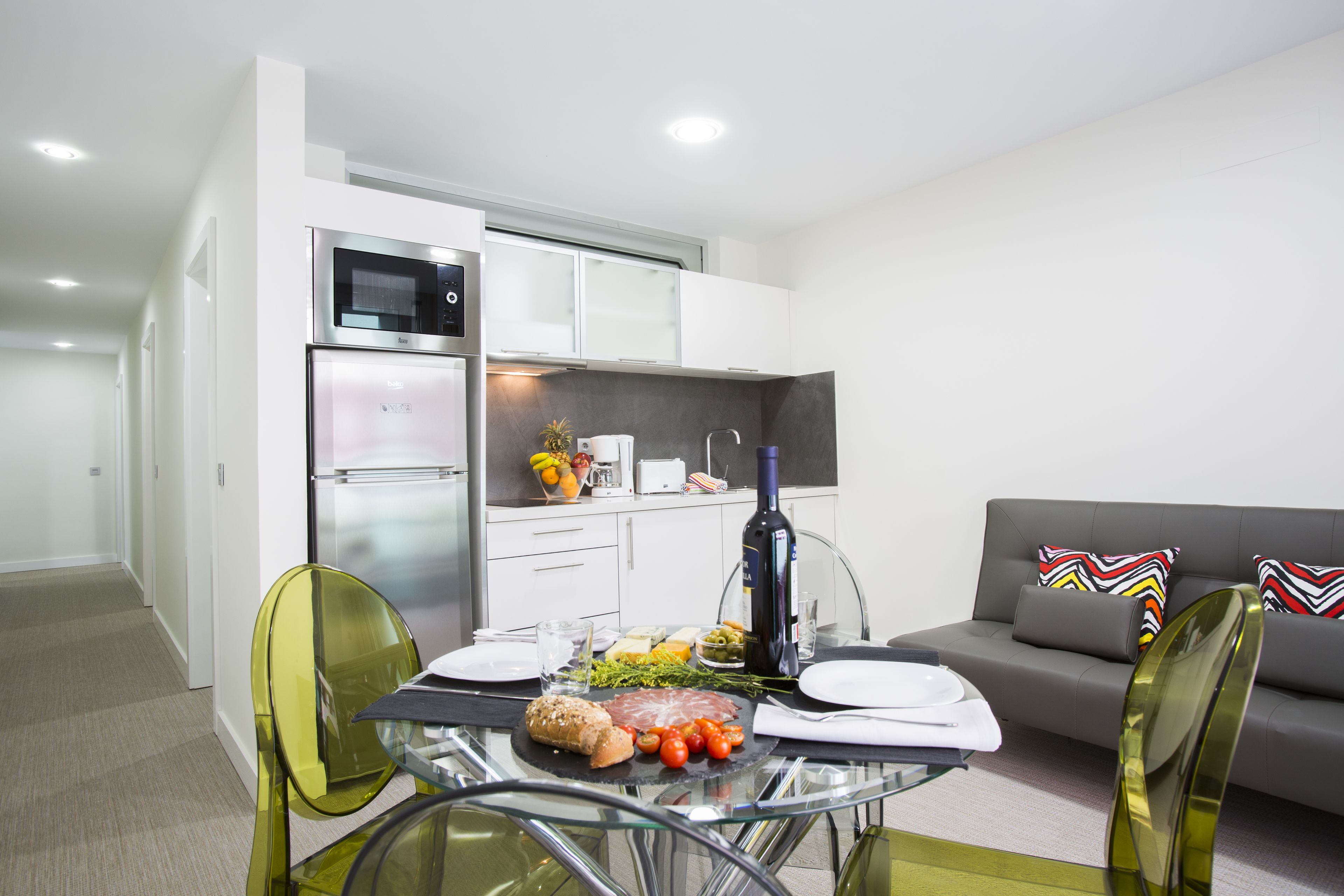 A modern kitchen with white cabinets, a built-in oven, and a dining area with a glass table and chairs.