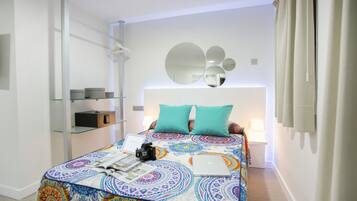 Une chambre à coucher moderne avec une couvre-lit à motifs, un ordinateur portable, un appareil photo et une lampe de chevet.