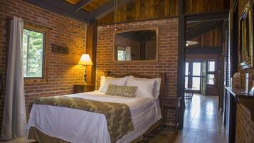 A room with a brick wall, a bed with a white and green bedspread, a nightstand with a lamp, and a large mirror on the wall.