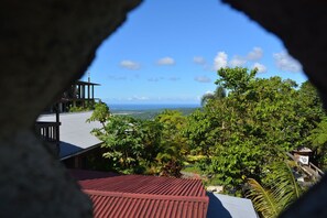 A view through a window with a red roof, overlooking a lush green landscape and a distant body of water. - Rainforest Inn (Río Grande)