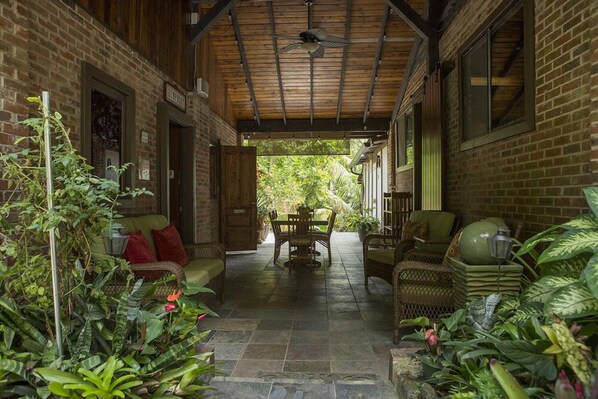 A covered patio with a brick wall, a wooden ceiling, and a table with chairs. - Rainforest Inn (Río Grande)