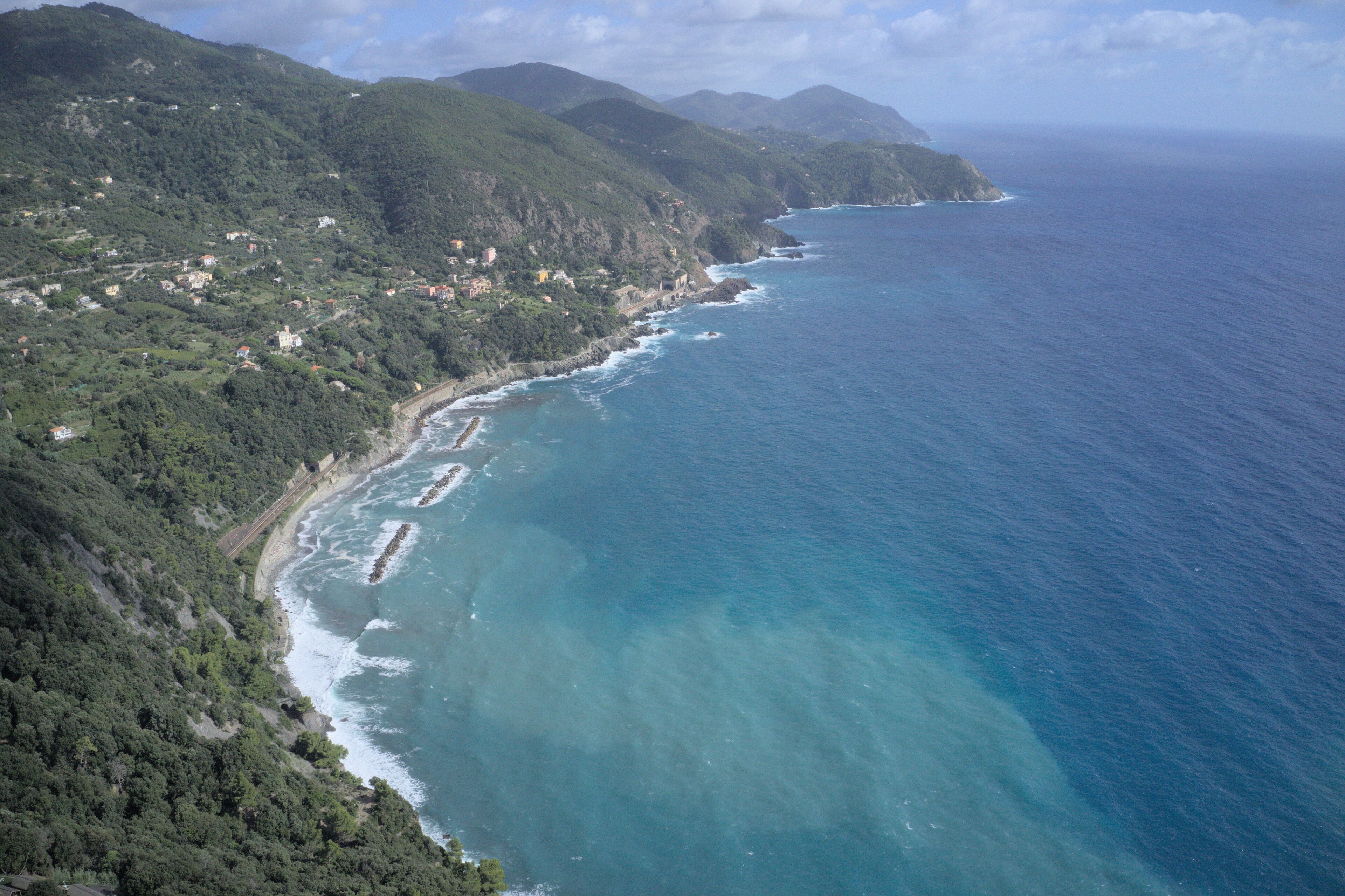 Un paysage côtier caractérisé par une étroite bande de terre qui mène à la mer, entourée de collines et parsemée de bâtiments.