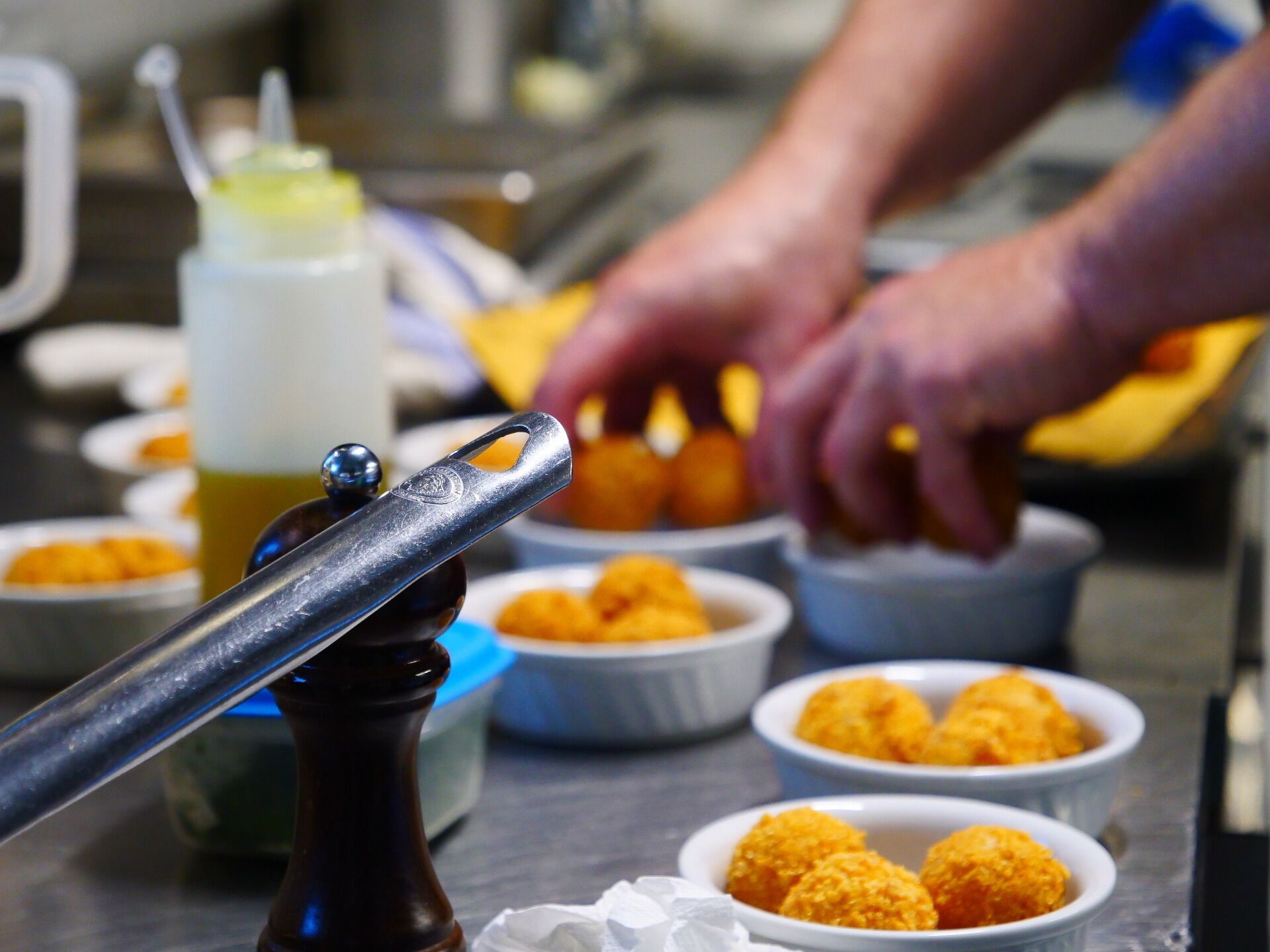 A kitchen counter with a pepper mill, bowls of food, and a person preparing food.
