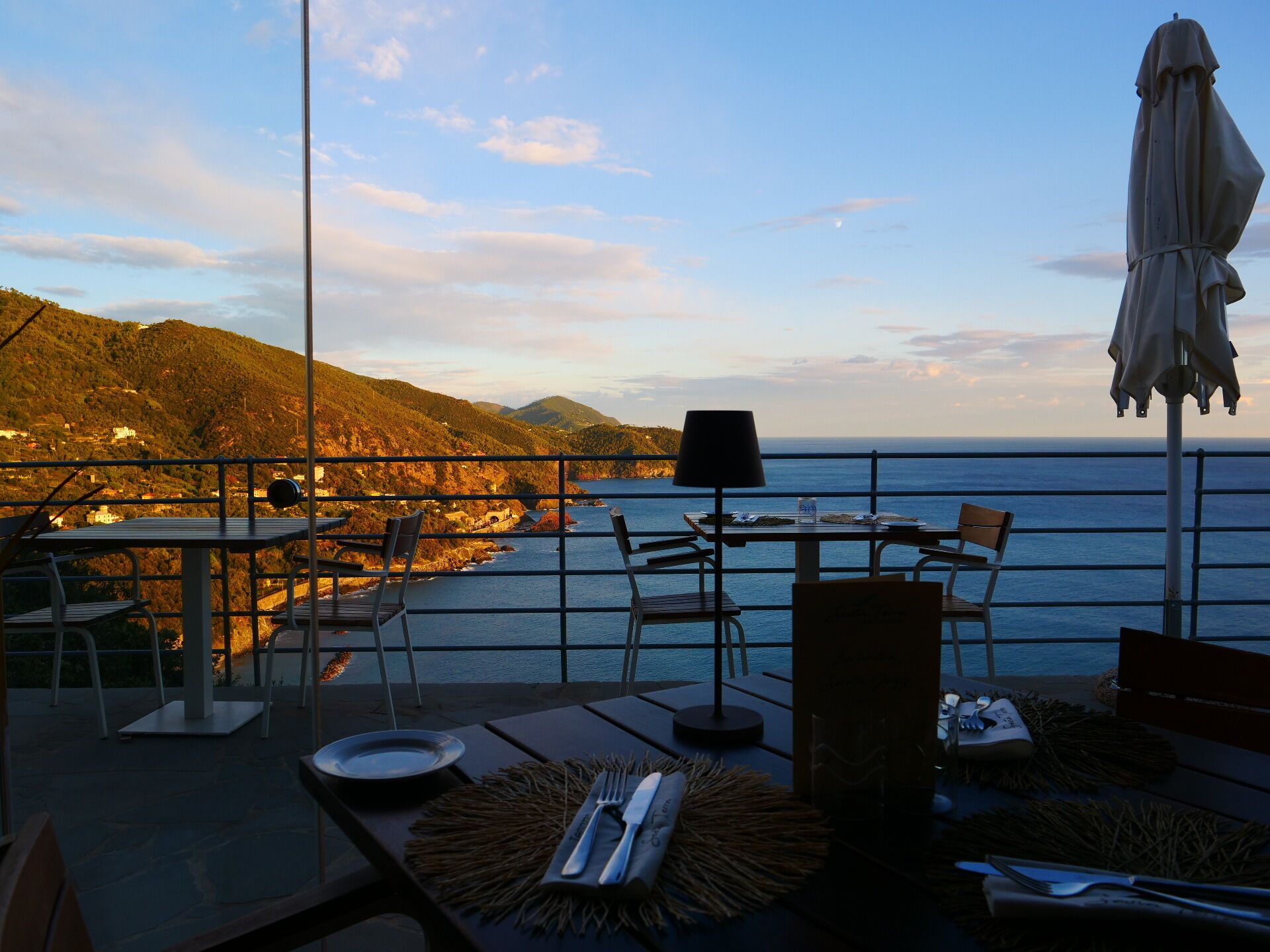 Una terrazza con tavoli e sedie che si affaccia su un paesaggio costiero con colline e il mare.