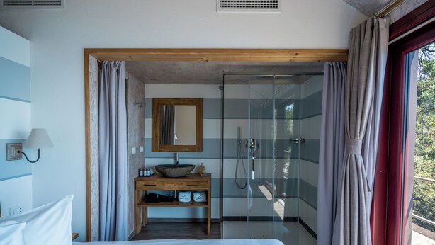 A bedroom with a bed, a wooden nightstand, a mirror, a sink, and a shower. - Sesta Terra Natural Resort (Framura)