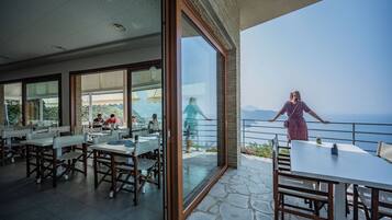 A dining area with tables and chairs, large windows, and a view of the sea.
