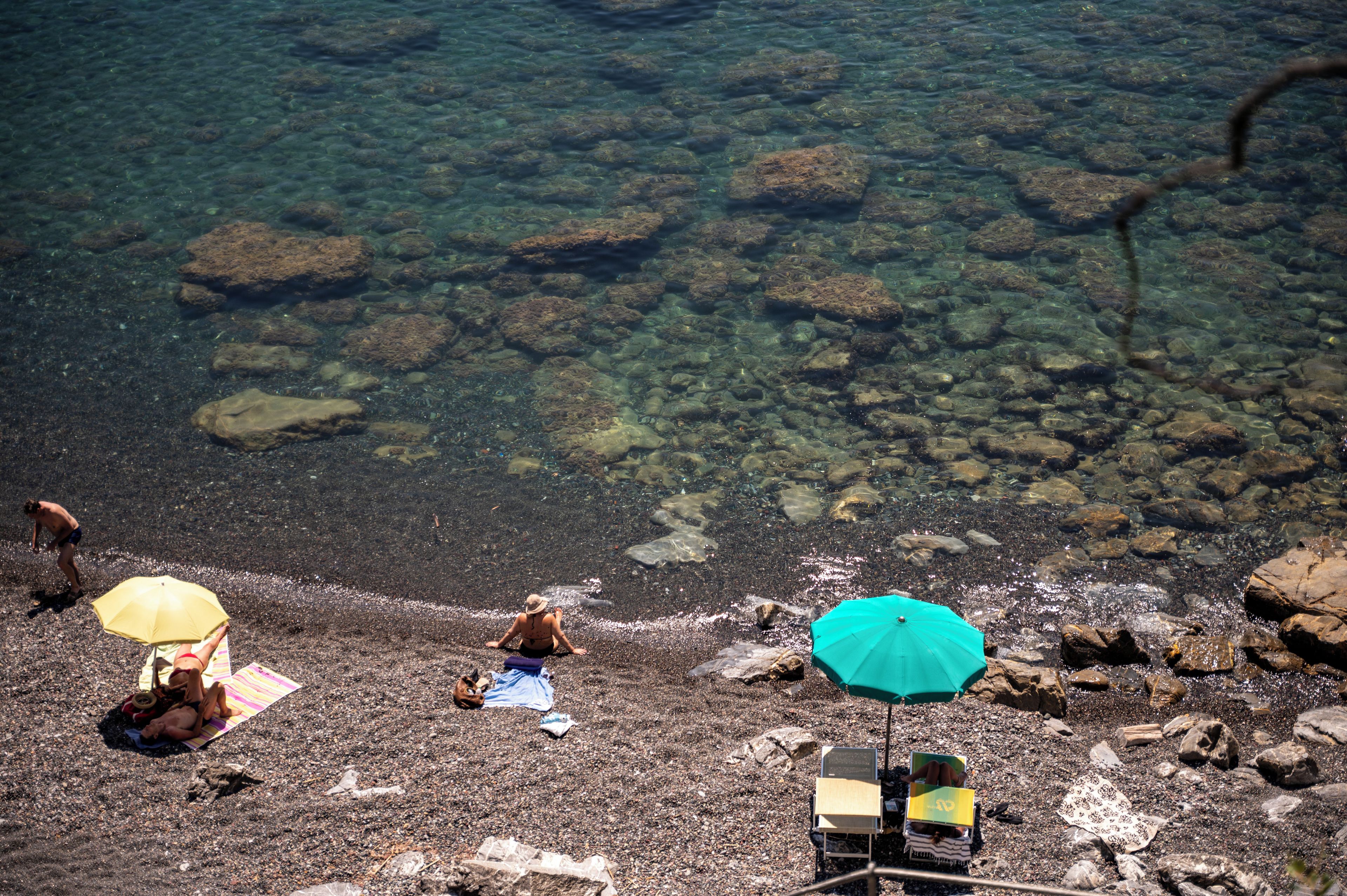 Une plage avec une eau claire, des rochers et des gens qui se détendent sous des parasols.
