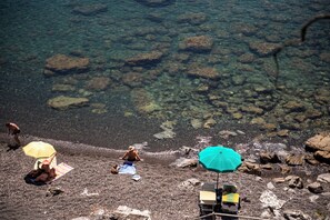 A beach with clear water, rocks, and people relaxing under umbrellas. - Sesta Terra Natural Resort (Framura)