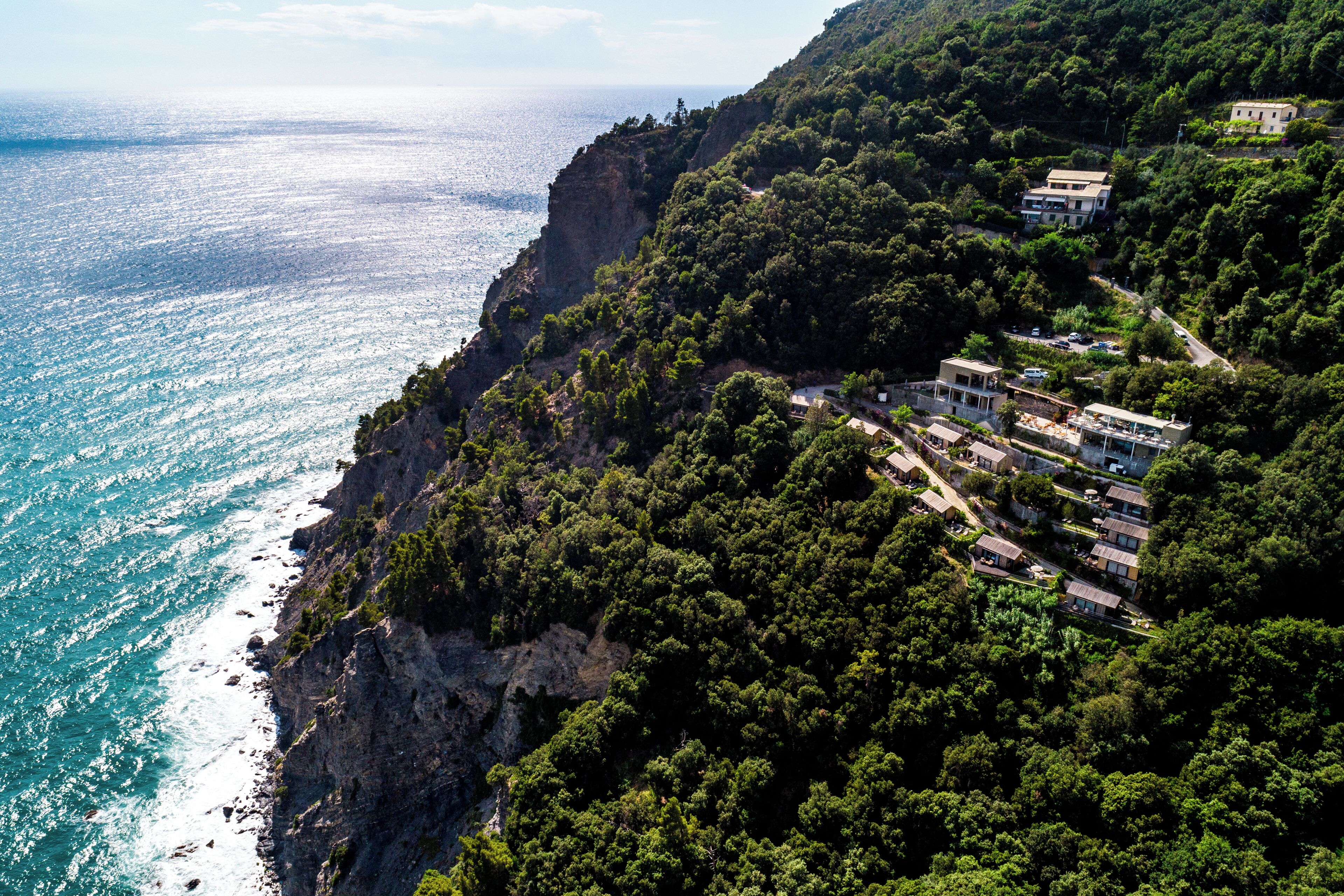 A coastal property with a cliffside view overlooking the sea, featuring multiple buildings and lush greenery.