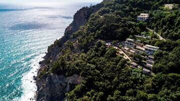 A coastal property with a cliffside view overlooking the sea, featuring multiple buildings and lush greenery.