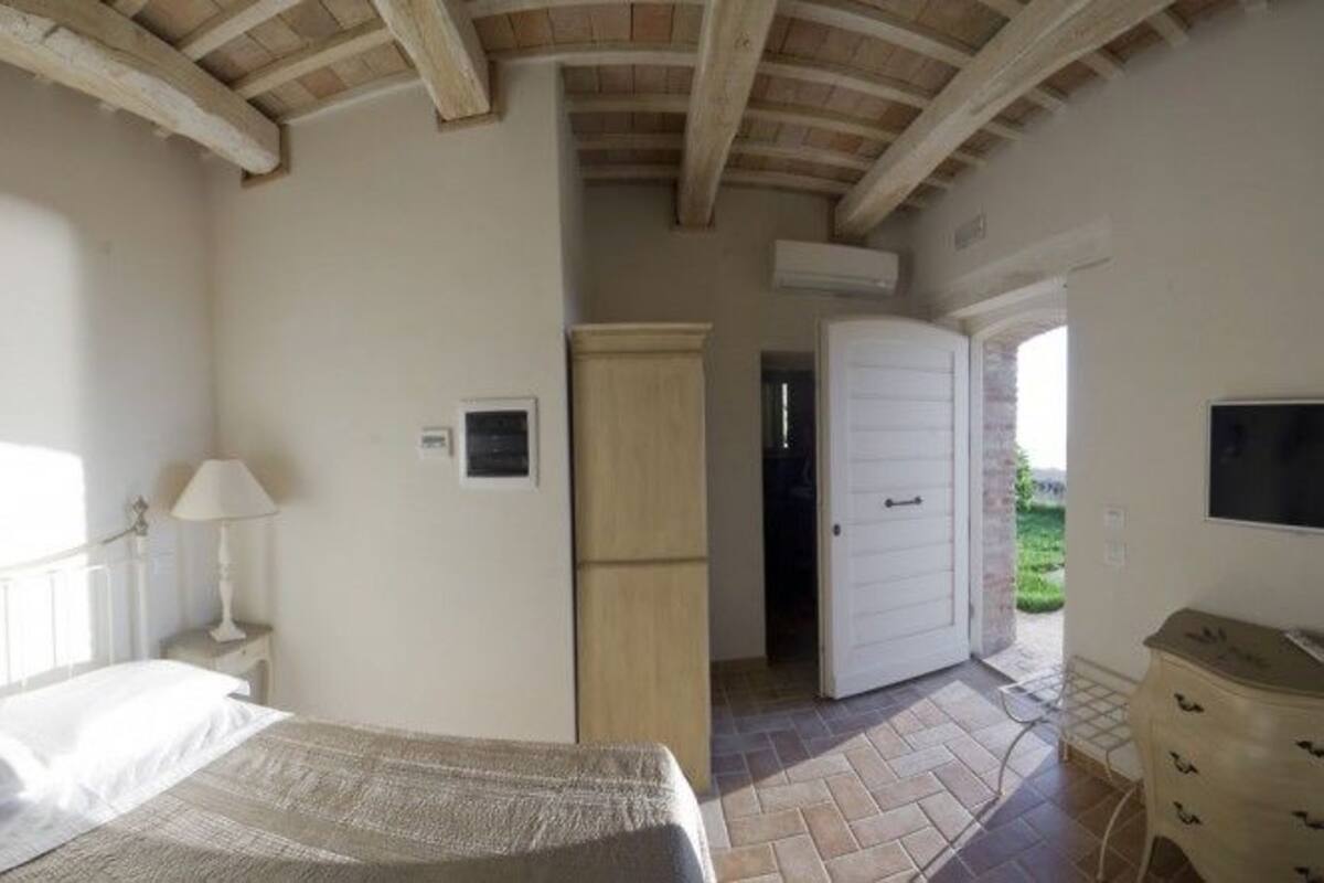 A bedroom with a bed, bedside lamps, a wardrobe, and a door leading to an outdoor area.