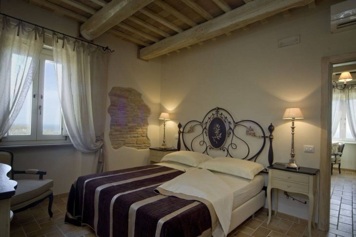 A bedroom with a double bed, two bedside tables with lamps, a chair, and a window with curtains.
