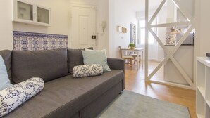 Una sala moderna con un sofá gris, cojines estampados, un salpicadero de azulejos y vistas al comedor.