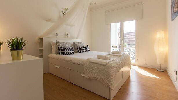 Un dormitorio con cama, mesitas de noche, una planta en maceta y vistas al exterior.