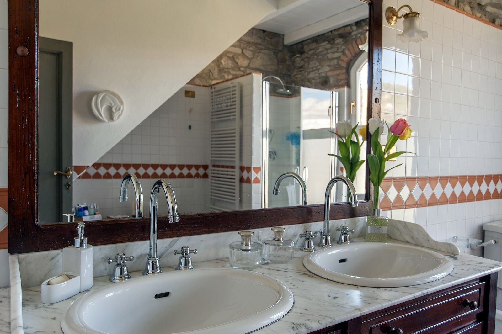 Ein Badezimmer mit zwei Waschbecken, einem großen Spiegel und einer Blumenvase.