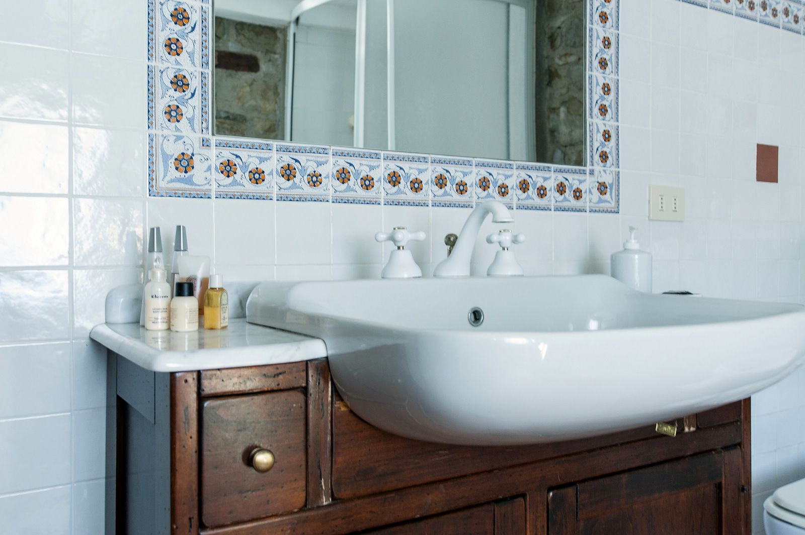 Un baño con lavamanos blanco, mueble de madera y un borde decorativo de azulejos.