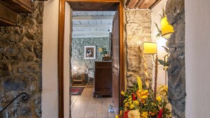 A stone-walled hallway leading to a room with a wooden ceiling, a wooden cabinet, and a floral arrangement. - Fattoria Ca' di Fatino (Castiglione dei Pepoli)