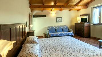 Un dormitorio con techo de madera, una cama con ropa de cama floral, un sofá, un aparador y una ventana con cortinas.
