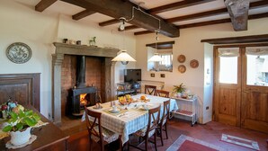 A dining area with a fireplace, wooden beams, and a table set for a meal. - Fattoria Ca' di Fatino (Castiglione dei Pepoli)