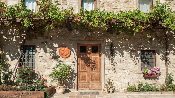 A stone building with a wooden door, potted plants, and a small window with a curtain. - Fattoria Ca' di Fatino (Castiglione dei Pepoli)