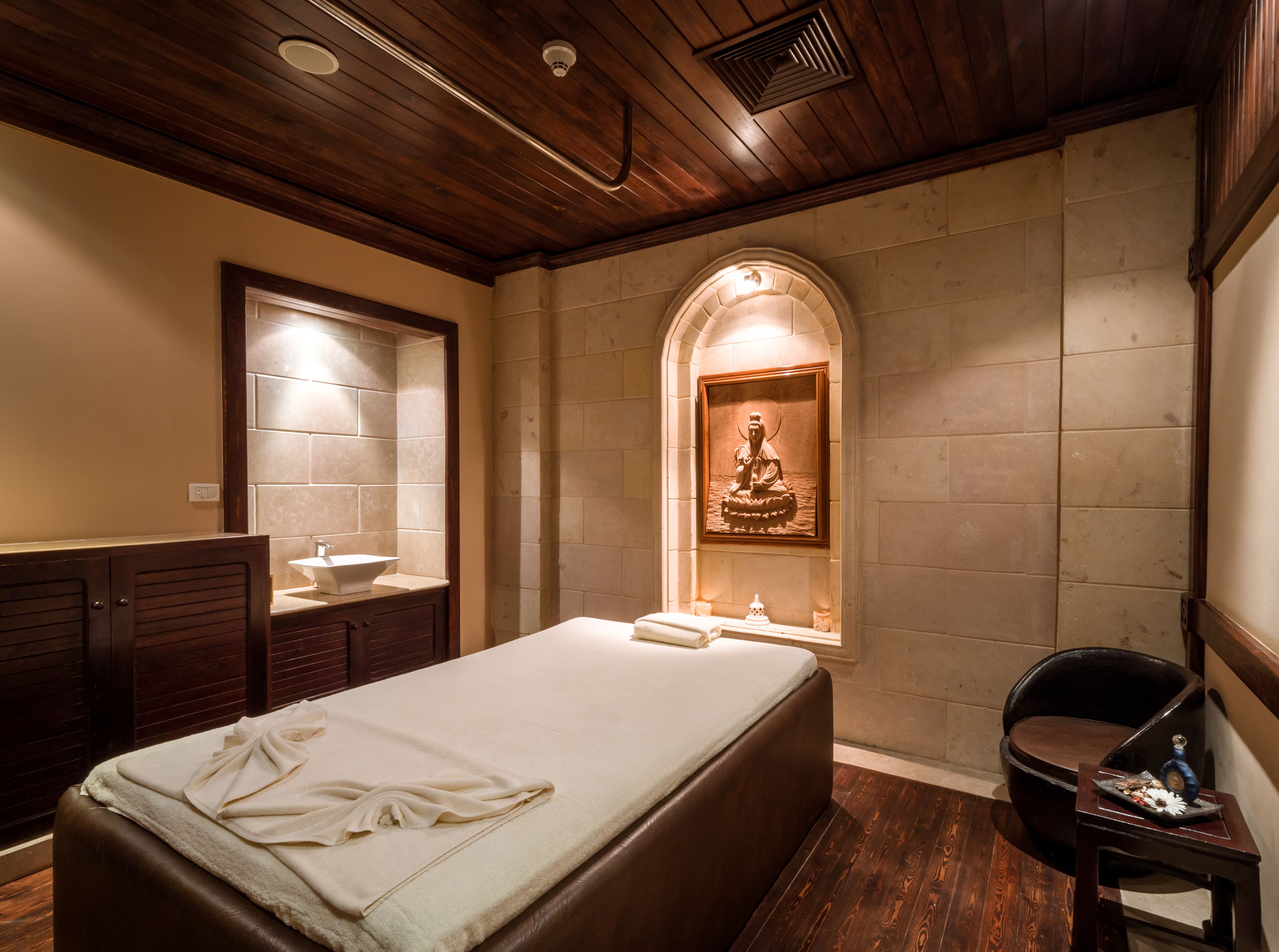 Une chambre d’hôtel avec un lit, une coiffeuse avec un miroir, un lavabo et une statue.
