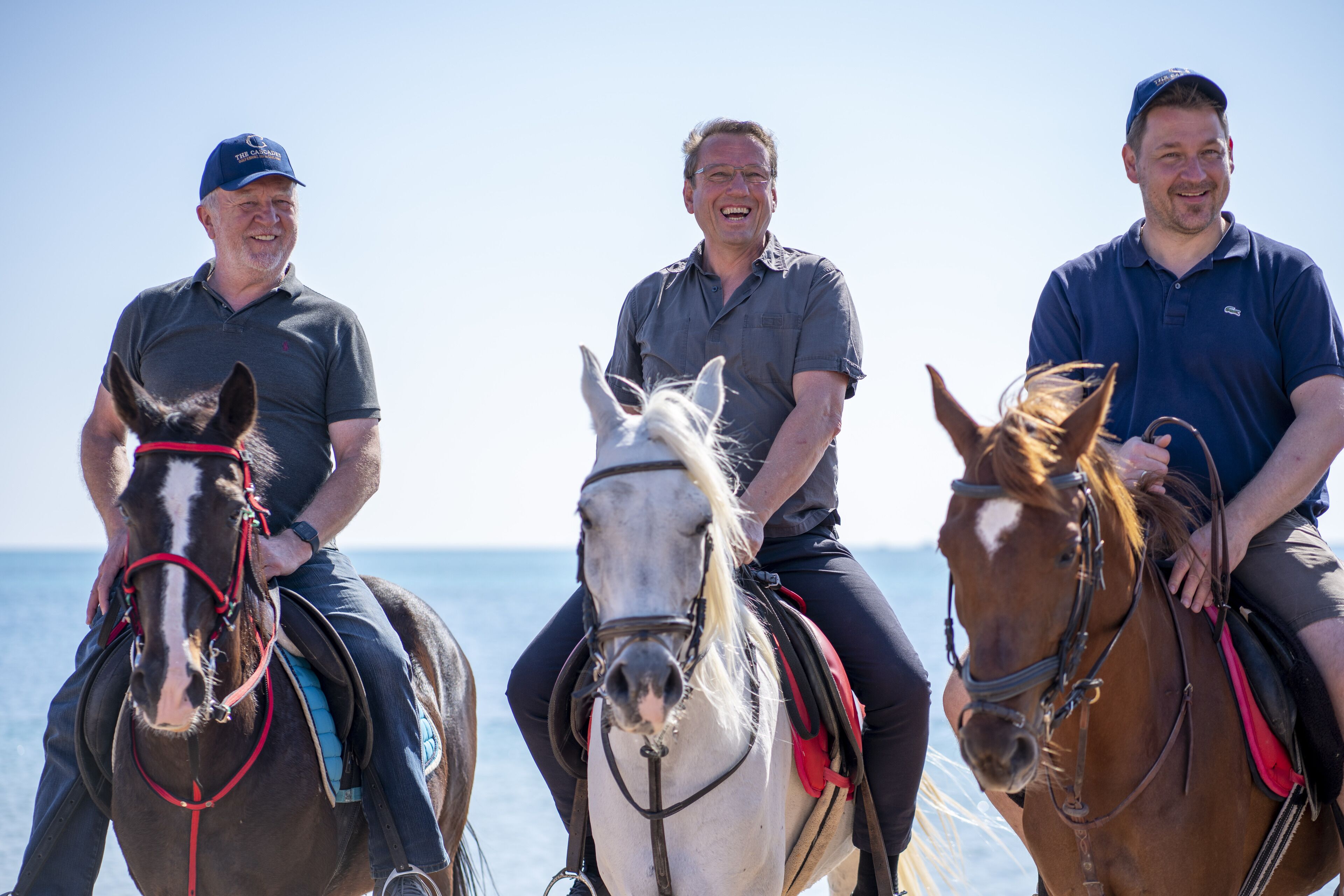 Three men on horses by the sea.