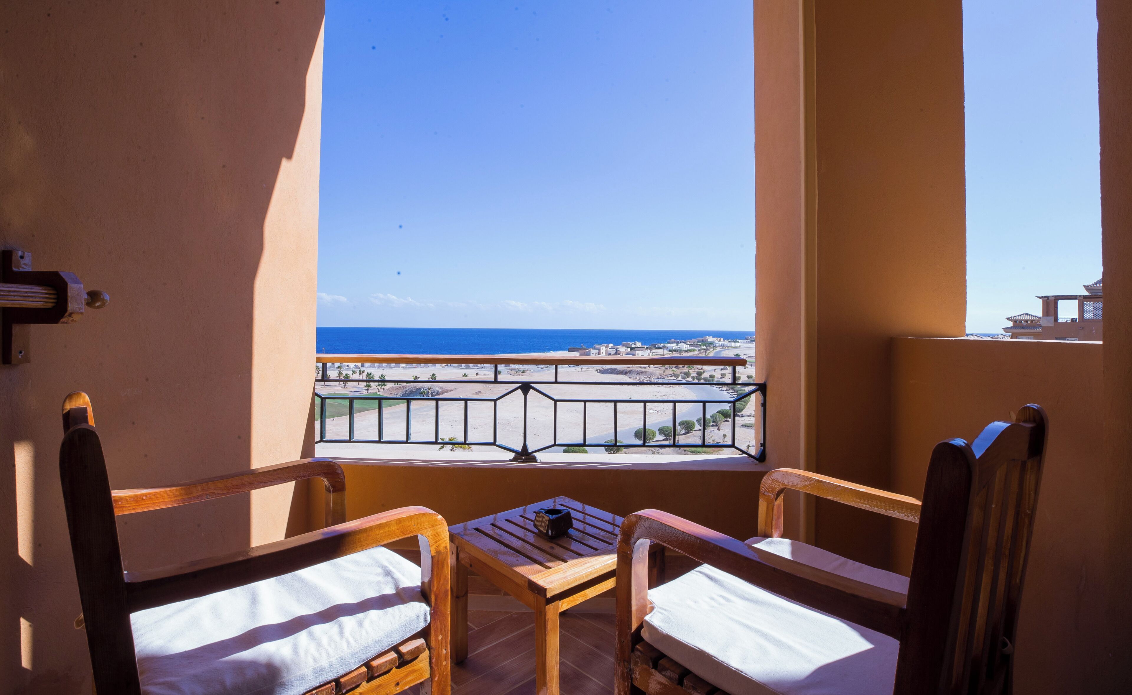 A balcony with two wooden chairs and a small table, overlooking a beach and ocean.