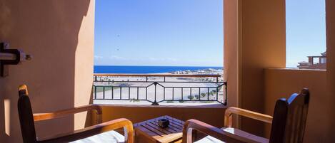 A balcony with two wooden chairs and a small table, overlooking a beach and ocean.
