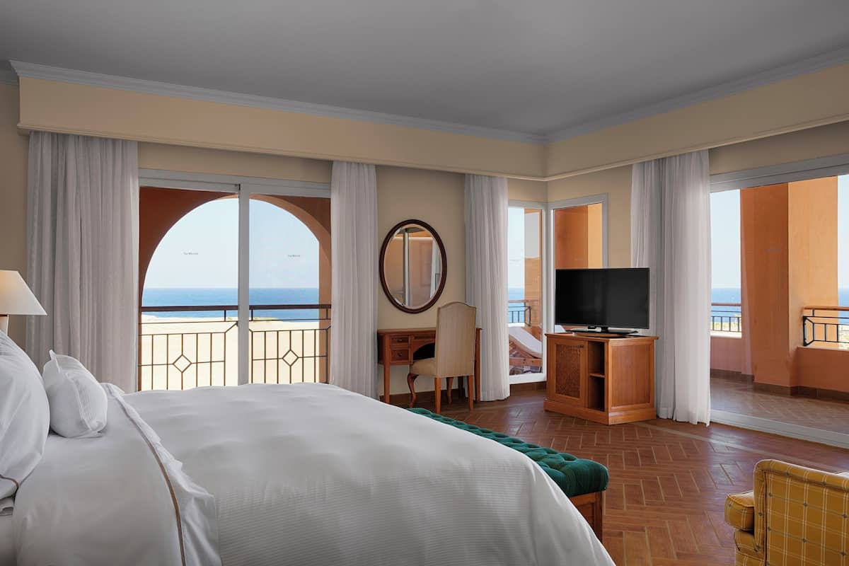 Une chambre d’hôtel avec un grand lit, un bureau avec une chaise, une télévision et une vue sur l’océan.