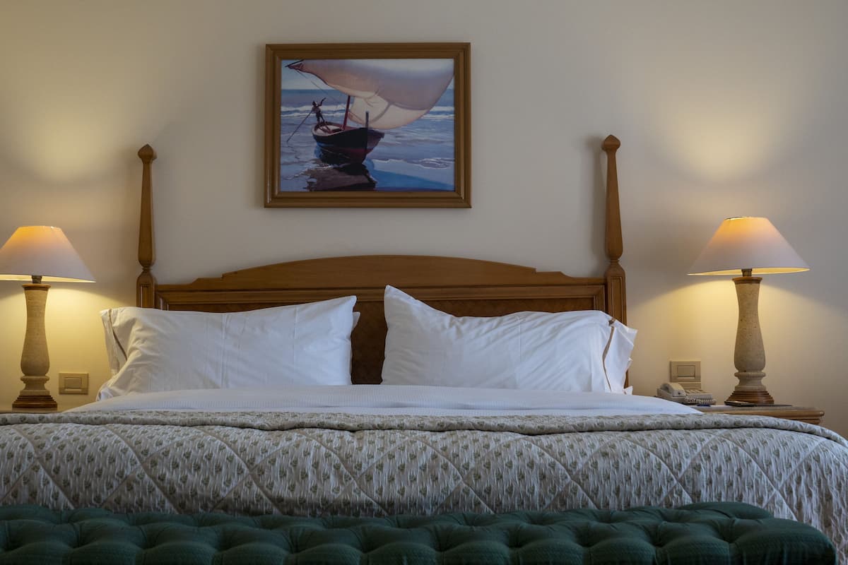 Un lit bien fait, recouvert d’une couvre-lit à motifs floraux, avec deux lampes de chevet et un tableau encadré représentant un voilier accroché au mur.