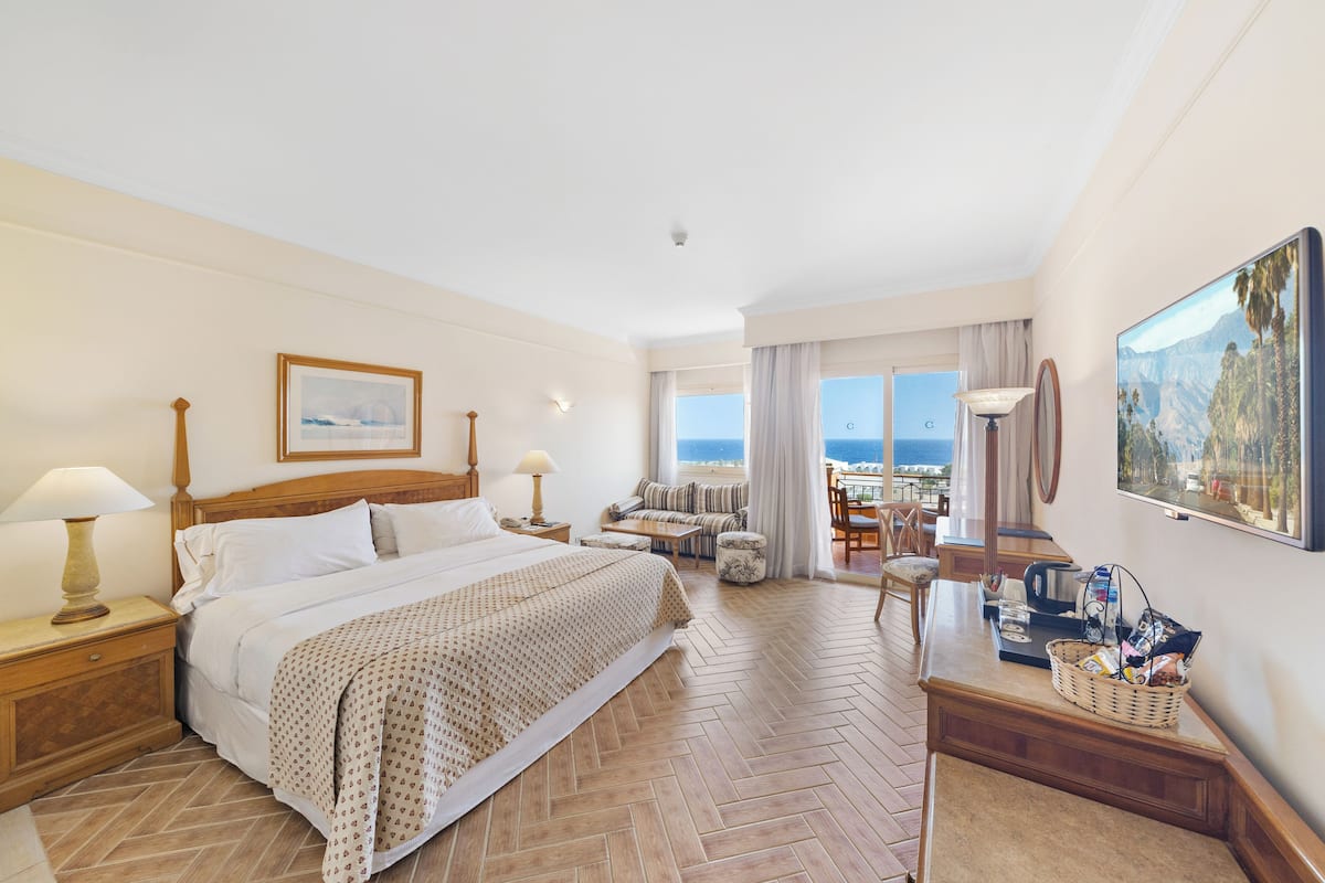 Une chambre d’hôtel avec un lit, un bureau, une chaise, une table et une vue sur l’océan.