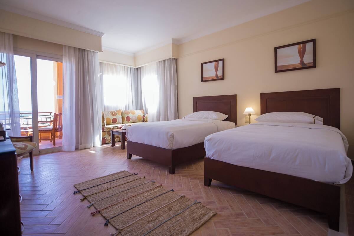 Une chambre d’hôtel avec deux lits, un bureau et une chaise. On peut admirer la vue sur l’extérieur à travers une porte coulissante.