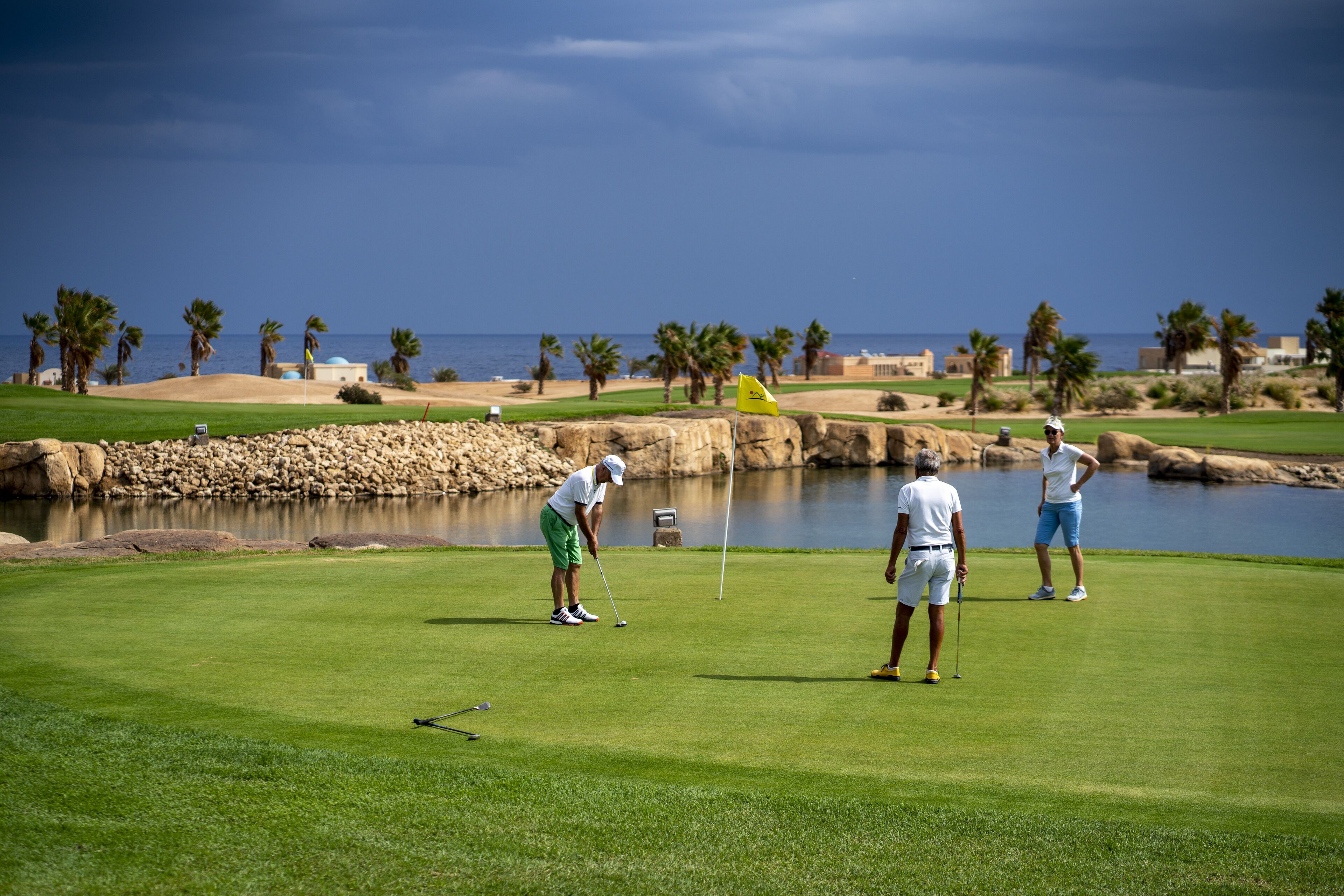 Un campo de golf con un cuerpo de agua, palmeras y un cielo despejado.