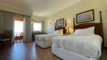 Quarto de hotel com duas camas, piso de madeira, área de refeições com mesa e cadeiras, e janela com cortinas.