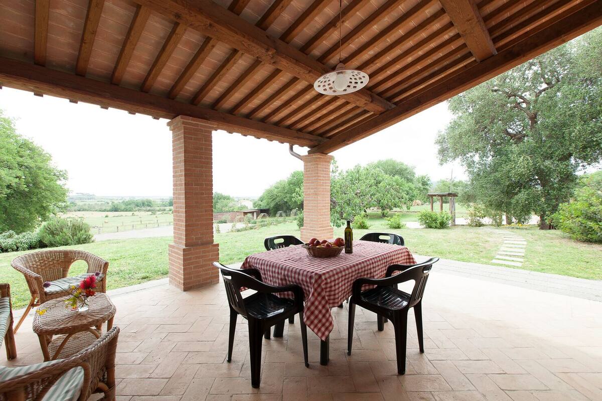 An outdoor patio with a brick table and chairs, a wicker chair, and a view of a grassy area with trees.