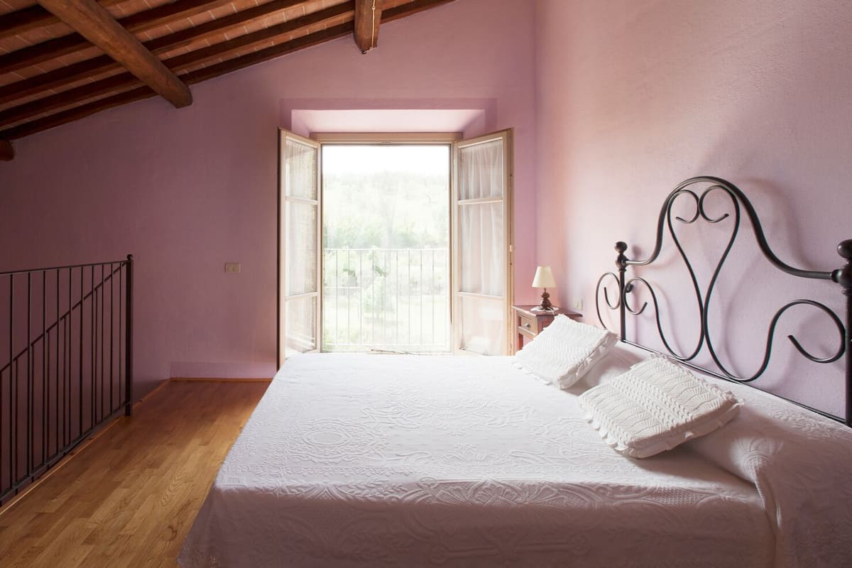 A bedroom with a large bed, a wooden floor, a metal headboard, and a window with curtains.