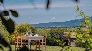 A dining table set outdoors with chairs, surrounded by greenery and a view of distant mountains. - Agriturismo Bio Podere Doganelle (Gavorrano)