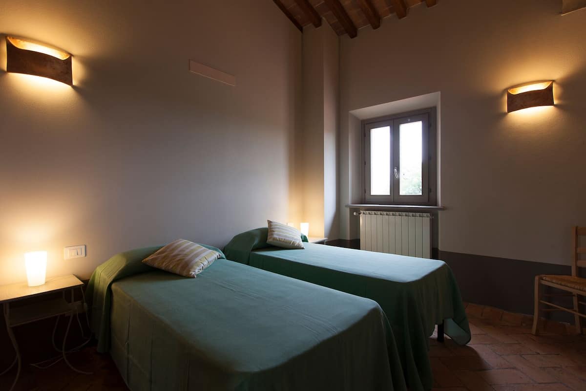 A room with two single beds, a window, a radiator, and wall-mounted lights.