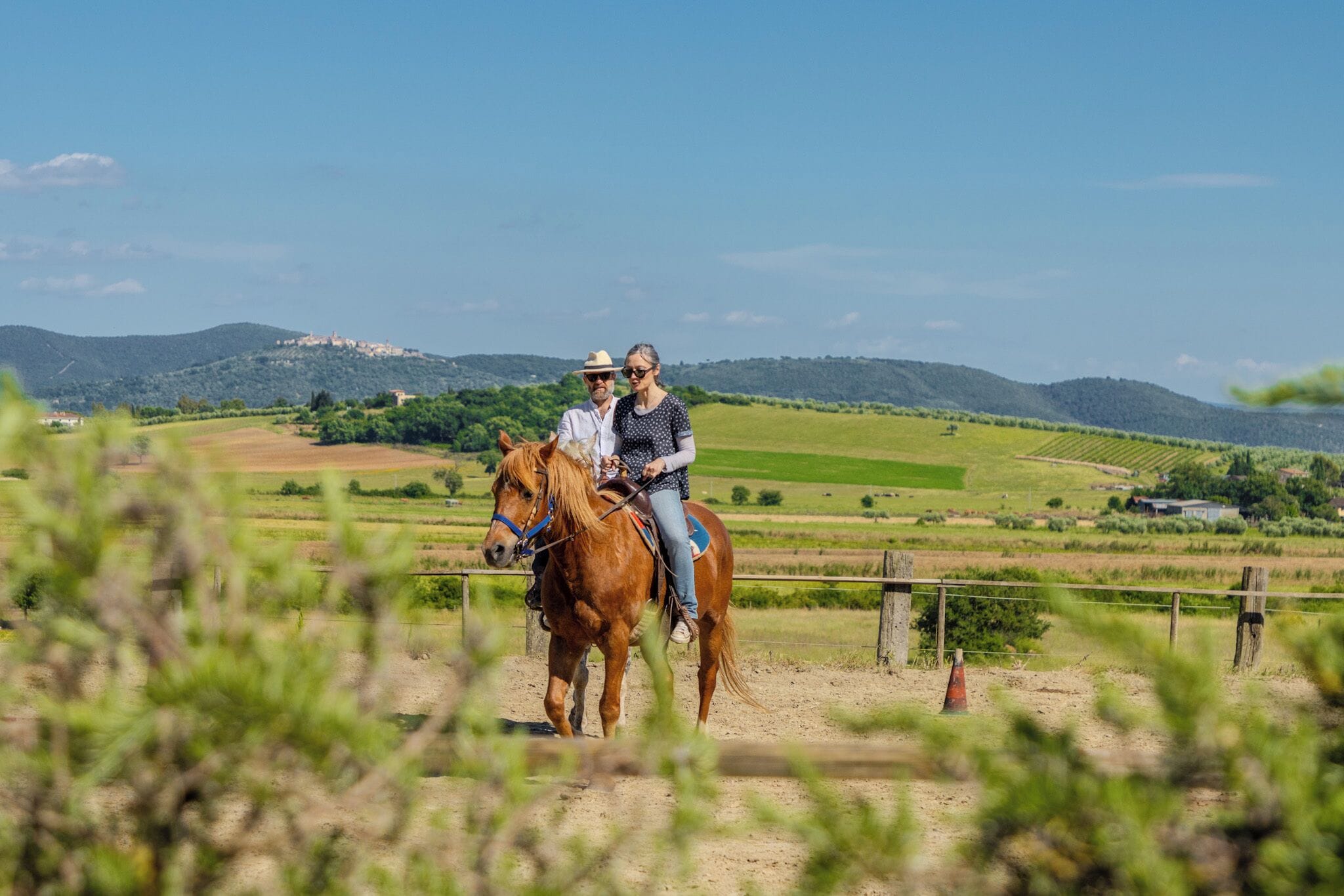 A person riding a horse in a fenced area with a hilly landscape in the background.