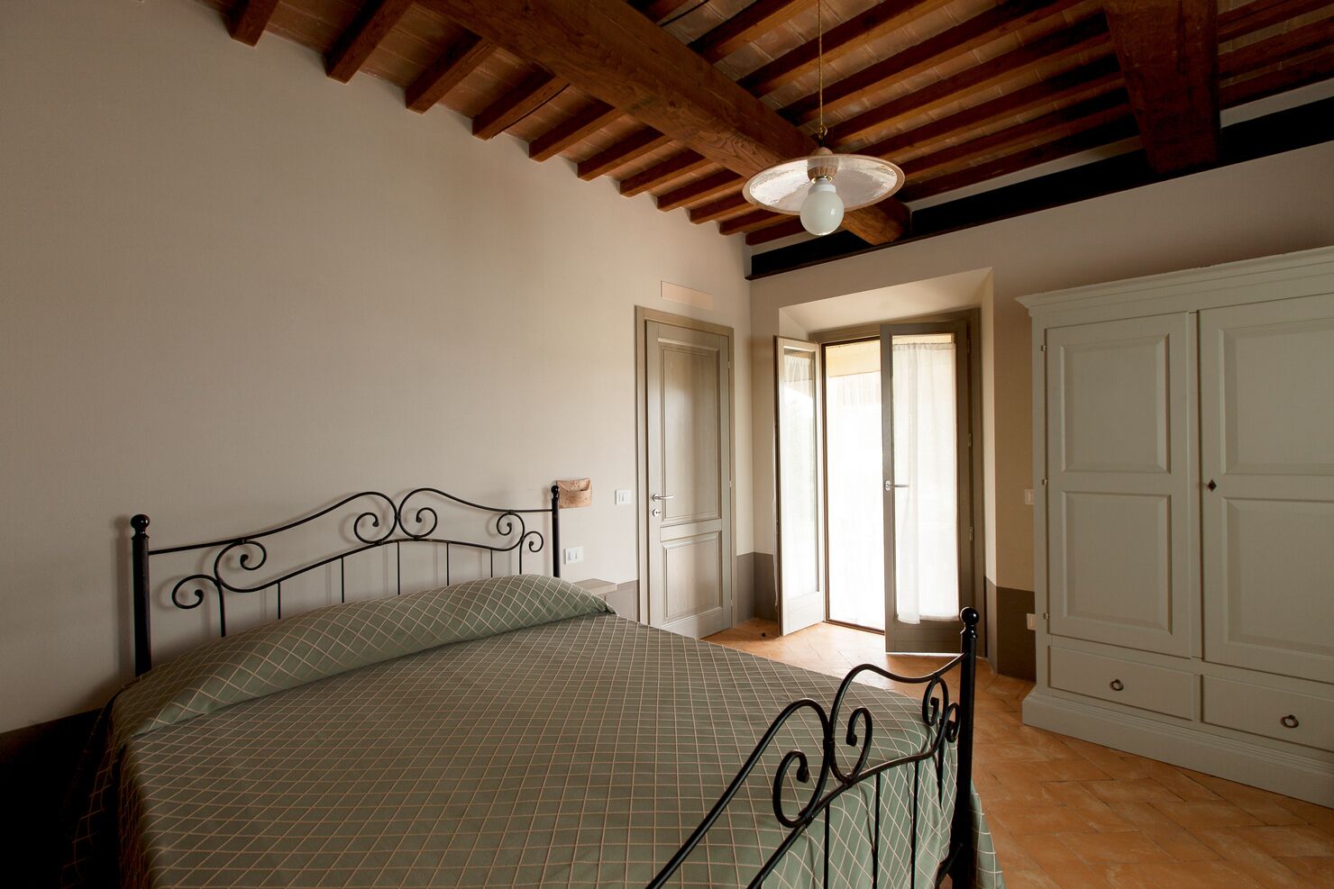 A bedroom with a bed, wooden ceiling beams, a door, and a wardrobe.