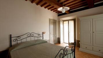 A bedroom with a bed, wooden ceiling beams, a door, and a wardrobe.