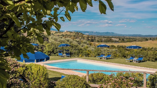 A pool area with lounge chairs and umbrellas, surrounded by greenery and hills in the background. - Agriturismo Bio Podere Doganelle (Gavorrano)