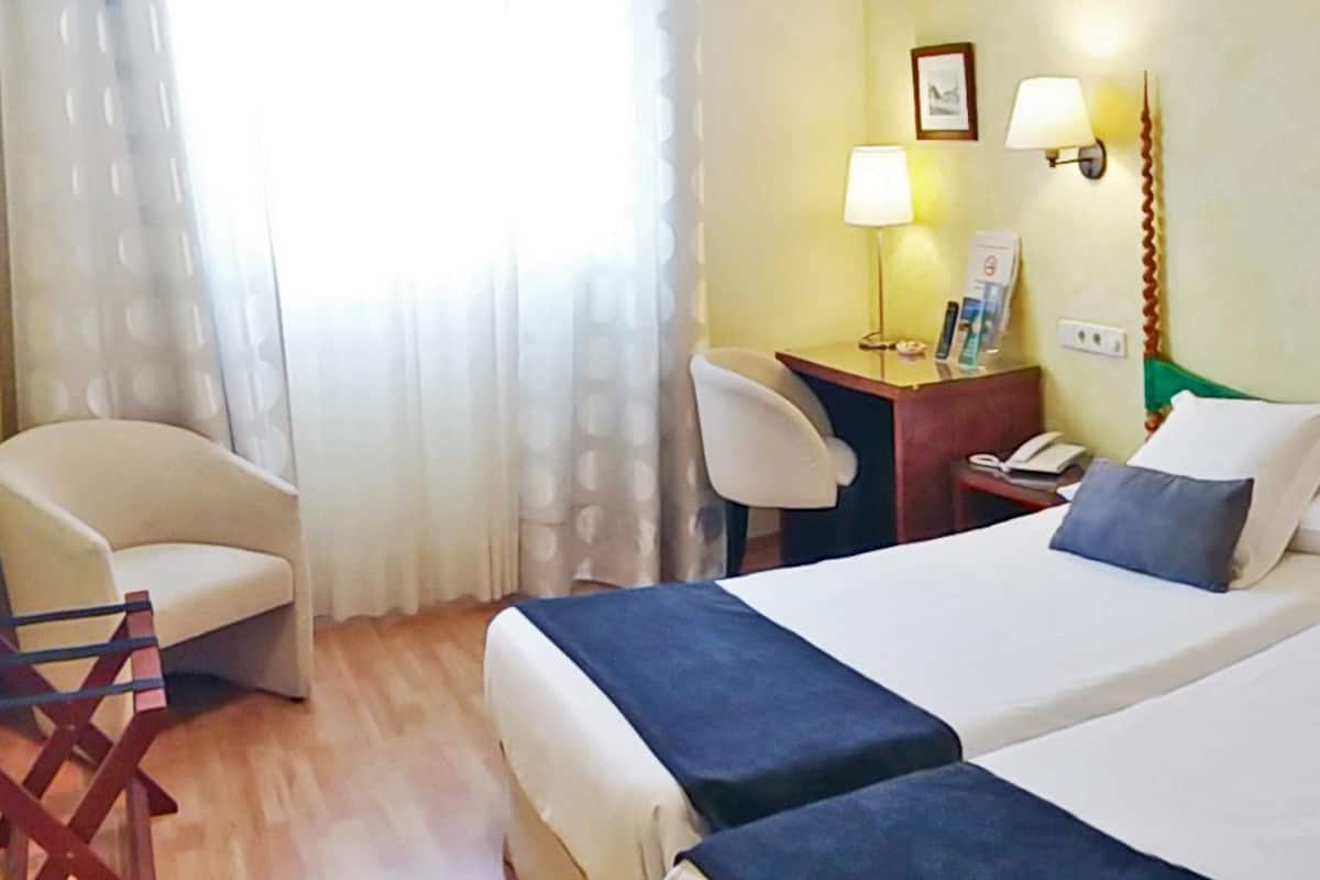 Habitació d'hotel amb dos llits, un escriptori, una cadira i una finestra amb cortines.