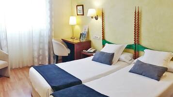 A hotel room with two beds, a desk, a chair, and a window with curtains.