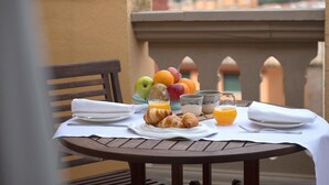 Taula preparada amb croissants, fruita i suc a un balcó amb vista a edificis i muntanyes.
